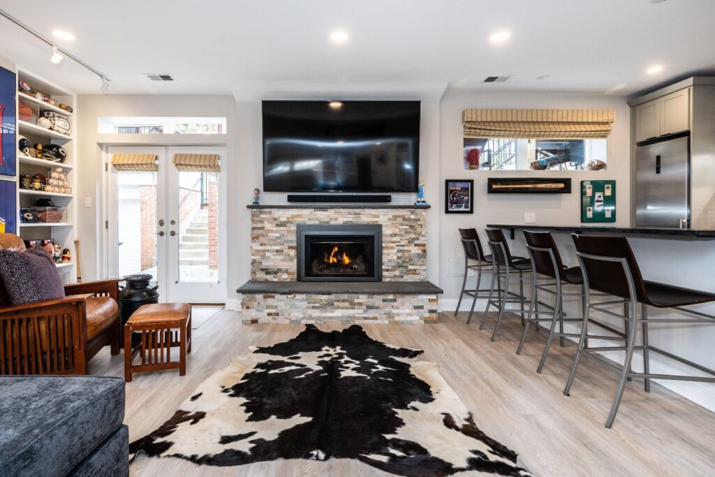This basement remodeling project features a stylish family room with a stone fireplace, full-service bar, and custom sports memorabilia display located in Palisades, Washington, DC, - designed and built by Spectrum Design + Build.